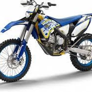 Può includere: Una moto Husqvarna blu e bianca con una sella gialla e ruote nere. La moto è una moto da cross con uno scarico montato in alto.