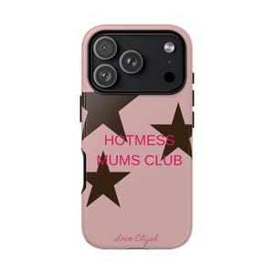 以下が含まれることがあります： ピンク色の携帯電話ケース。ピンク色の「HOTMESS MUMS CLUB」の文字と茶色の星のグラフィックが特徴です。ケースには黒いカメラモジュールと、下部に「Love Elijah」のサインがあります。