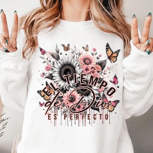 May include: White sweatshirt with a floral design and the text "EL TIEMPO de DIOS ES PERFECTO" in pink and black lettering.