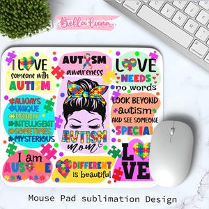 May include: A white mouse pad with a colorful design promoting autism awareness. The design includes puzzle pieces, hearts, and text such as "Love," "Autism Awareness," and "Different is beautiful." A computer mouse and keyboard are visible.