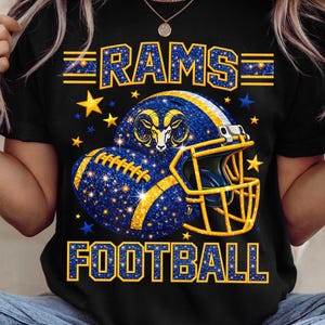 May include: Black t-shirt with a graphic design featuring the word "RAMS" above a football helmet and football, with the word "FOOTBALL" below. The design is in blue and gold with star accents.