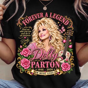 May include: A black t-shirt featuring a graphic of Dolly Parton with blonde hair, surrounded by pink roses, a butterfly, and an acoustic guitar. Text includes "FOREVER A LEGEND," "Dolly PARTON," "1946-2026," and "HER MUSIC LIVES ON" in pink and gold.