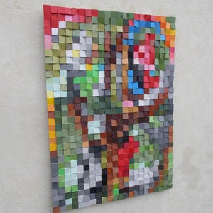Puede incluir: Un arte de pared abstracto colorido en mosaico hecho de pequeños cuadrados de madera en varios tonos de verde, rojo, azul, marrón y blanco.