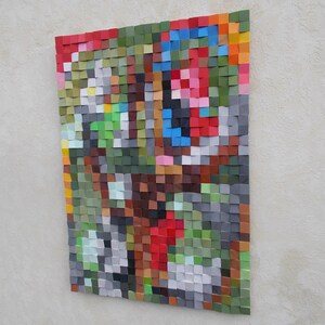 May include: Abstract wall art made of small wooden squares in various colors, including red, green, blue, and gray. The squares are arranged in a geometric pattern, creating a modern and colorful design.