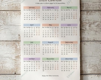 May include: A 2026 calendar with a wooden background, featuring monthly grids with dates. The calendar is suspended by a twine string. The text "A new year is a blank page full of possibilities" is printed at the top. A small plant and a mug are on the shelf below.