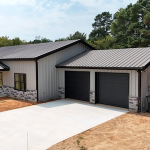 May include: A modern, single-story house with a metal roof and a two-car garage. The house is painted white with black trim and has a stone facade. The garage doors are black and the driveway is concrete.