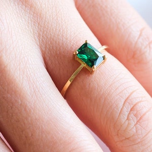 May include: A gold ring with a large, emerald green square-shaped gemstone.