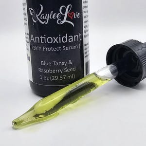 May include: A brown glass bottle with a dropper, labelled "Kaylee Love Antioxidant (Skin Protect Serum)". The bottle contains a green liquid and is labelled with "Blue Tansy & Raspberry Seed 1 oz (29.57 ml)".