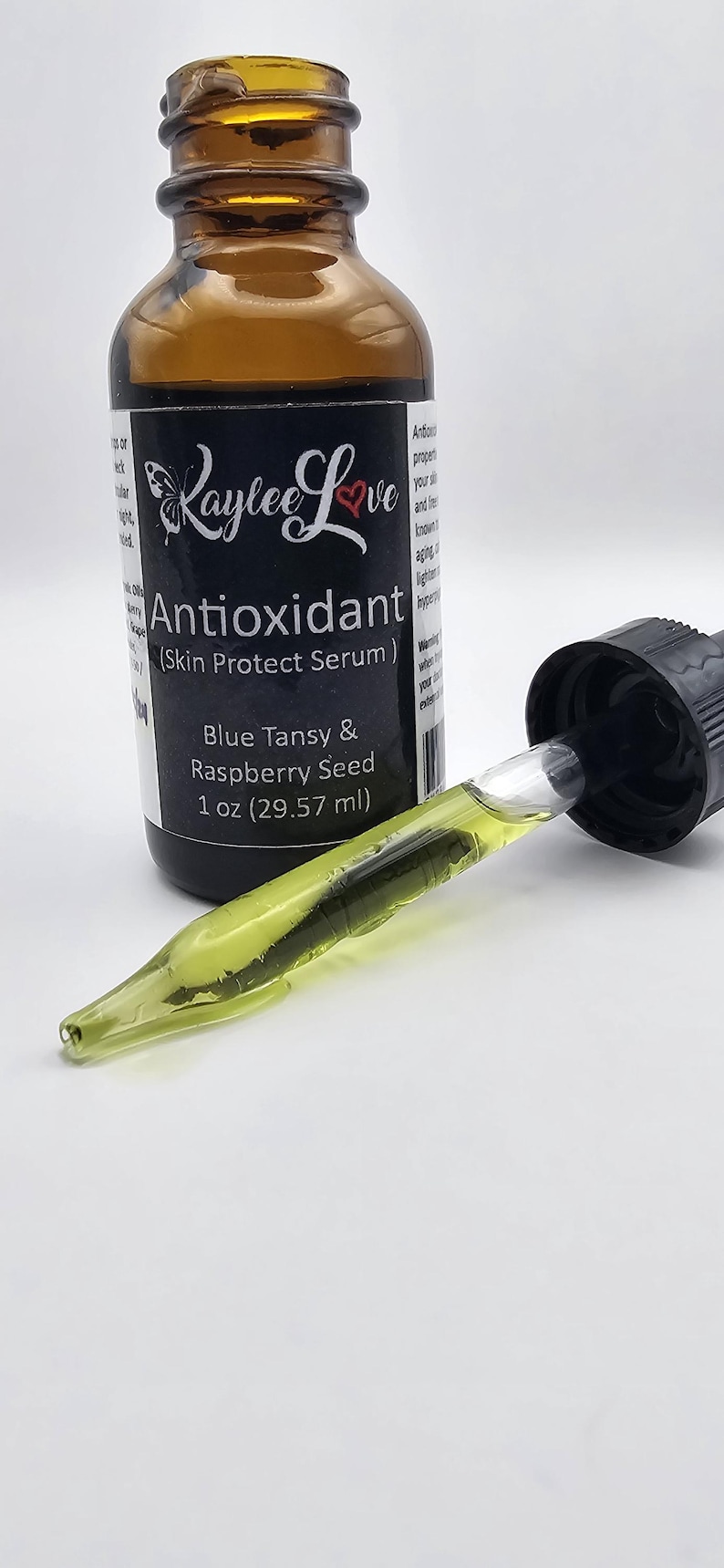 May include: A brown glass bottle with a dropper, labelled "Kaylee Love Antioxidant (Skin Protect Serum)". The bottle contains a green liquid and is labelled with "Blue Tansy & Raspberry Seed 1 oz (29.57 ml)".