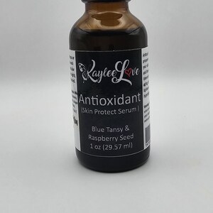 May include: A brown glass bottle with a black dropper top and a white label that reads "Raylee Love Antioxidant (Skin Protect Serum) Blue Tansy & Raspberry Seed 1 oz (29.57 ml)"