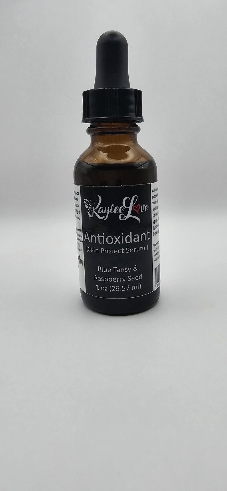 May include: A brown glass bottle with a black dropper top and a white label that reads "Raylee Love Antioxidant (Skin Protect Serum) Blue Tansy & Raspberry Seed 1 oz (29.57 ml)"