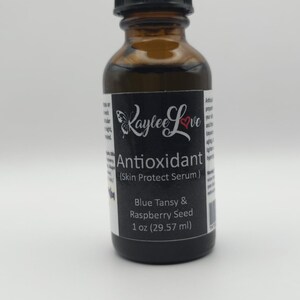 May include: A brown glass bottle with a black dropper top. The label is black with white text that reads "Raylee Love Antioxidant (Skin Protect Serum) Blue Tansy & Raspberry Seed 1 oz (29.57 ml)"