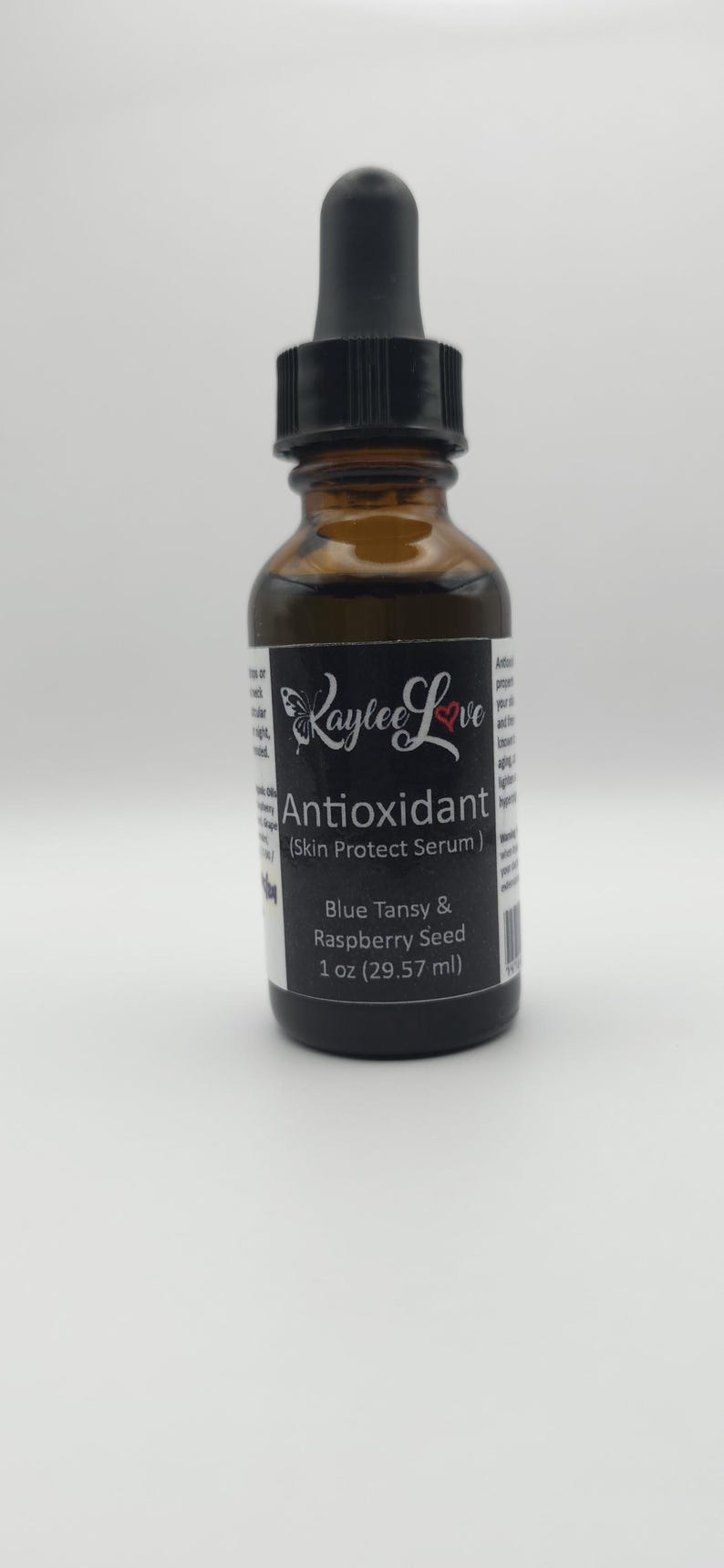 May include: A brown glass bottle with a black dropper top. The label is black with white text that reads "Raylee Love Antioxidant (Skin Protect Serum) Blue Tansy & Raspberry Seed 1 oz (29.57 ml)"