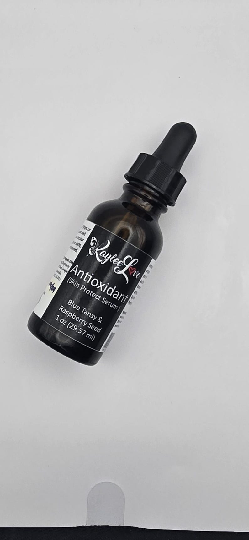 May include: A dark brown glass bottle with a black dropper top, labelled "Antioxidant (Skin Protect Serum)" with the brand name "Kaylee Love" and the text "Blue Tansy & Raspberry Seed 1 oz (29.57 ml)".