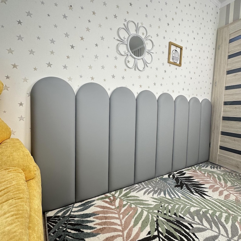 May include: A gray upholstered headboard featuring a series of vertical panels with rounded arched tops. The headboard is composed of eight individual segments arranged side by side, creating a continuous scalloped edge along the top border.