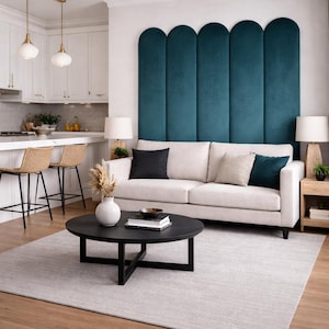 May include: A modern living room with a cream-colored sofa, black coffee table, and teal accent wall. The room features a light gray rug, wooden floors, and white kitchen cabinets with bar stools.