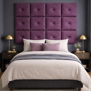 May include: A bedroom with a tufted, plum-colored headboard. The bed is made with a cream-colored comforter and gray throw. Two nightstands with gold lamps flank the bed. A light-colored rug is on the floor.