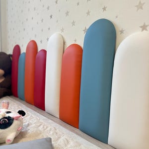 May include: A series of colourful, padded wall panels in red, orange, blue, and white. The panels are set against a wall decorated with stars, providing a decorative and practical feature for a child's room or play area.