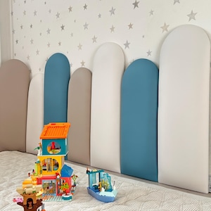 May include: A bedroom scene featuring a headboard with alternating panels of beige, white, and teal. A Lego house, boat, and other structures are on the bed. The wall is decorated with a pattern of gray stars.