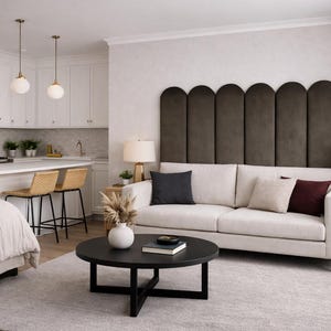 May include: A modern living room with a white sofa, dark accent pillows, and a large, dark brown headboard. A round black coffee table sits in front of the sofa. The room has a neutral color palette with a light gray rug.