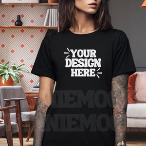 May include: A black t-shirt with the text "YOUR DESIGN HERE" printed in white on the front. The shirt is being modeled by a person with tattoos on their arm.