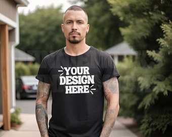 May include: A man wearing a black t-shirt with the text "YOUR DESIGN HERE" printed in white. He is standing in front of a house and some greenery.
