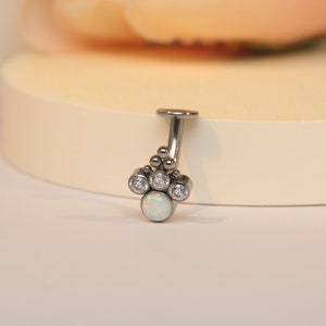 Puede incluir: Un piercing corporal de plata con una piedra de ópalo blanco y acentos de circonita cúbica transparentes.