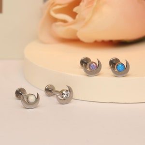 May include: Three silver crescent moon earrings with opal stones. The stones are white, blue, and purple.