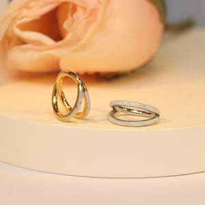 May include: Two hoop earrings, one gold and one silver, with a white opal inlay. The earrings are on a white surface.