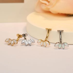 May include: Three surgical steel belly button rings with a five-leaf design. The rings are available in gold, silver, and opal.