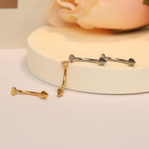 May include: Two pairs of surgical steel nose rings with a pointed end. One pair is gold and the other is silver.