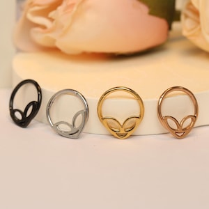 May include: Four different colored alien face hoop earrings. The hoops are made of metal and are available in black, silver, gold, and rose gold.