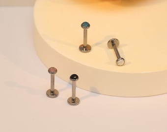 以下が含まれることがあります： 異なる色の宝石が付いた銀製のリップリングが4つ。宝石はターコイズ、ブラック、ピンク、ホワイトです。