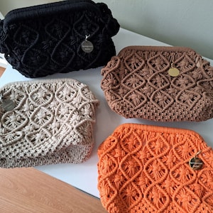Op de afbeelding: Vier gehaakte tassen in verschillende kleuren: zwart, beige, bruin en oranje. Elke tas heeft een klein rond label met het woord "Spring Blossom" erop.