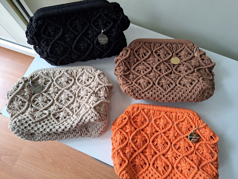 Op de afbeelding: Vier gehaakte tassen in verschillende kleuren: zwart, beige, bruin en oranje. Elke tas heeft een klein rond label met het woord "Spring Blossom" erop.