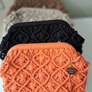 Op de afbeelding: Oranje gebreide clutch met een gouden label met de tekst "Springmoon Atelier".