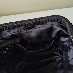 Op de afbeelding: Zwarte gehaakte tote bag met een zwarte satijnen voering. De tas heeft een ritssluiting en een geweven ontwerp.