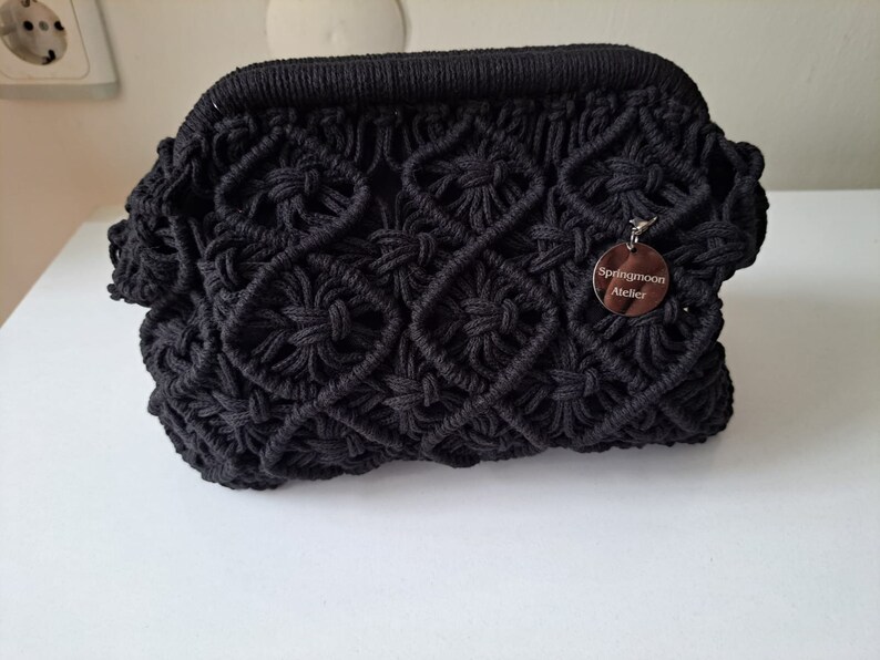 Op de afbeelding: Zwarte gecrochete tas met een zilveren label met de tekst "Springmoon Atelier".