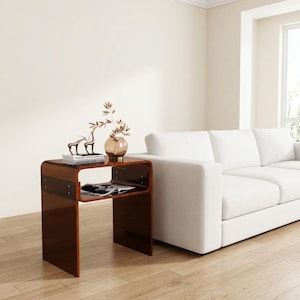 May include: A dark brown, translucent acrylic side table with a C-shaped design, featuring a flat top surface and a lower shelf. The table is constructed from curved, glossy material and includes visible metal hardware connecting the side panels.