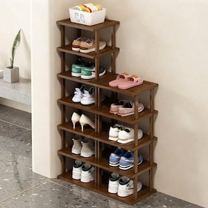 May include: A tiered wooden shoe rack with a dark brown finish, featuring multiple shelves arranged in a stepped configuration. The rack holds various styles of footwear, including sneakers, heels, and sandals, with a white storage bin on top.