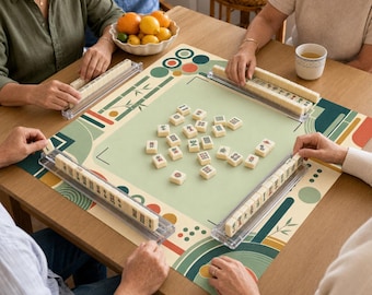 May include: A square mahjong game mat featuring a light green center with scattered white tiles, surrounded by a geometric pattern of circles and bamboo stalks in shades of green, orange, and cream, with four clear tile racks on the table.