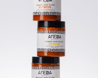 Könnte beinhalten: Drei Gläser ANEBA Naturals geschlagene Sheabutter, übereinander gestapelt. Die Gläser sind braun mit schwarzen Deckeln und weißen Etiketten. Das obere Glas ist mit "Ginger Vanilla" beschriftet, das mittlere Glas mit "Unscented" und das untere Glas mit "Strawberry Lemonade".