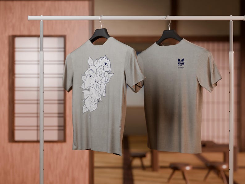 May include: Two gray t-shirts hanging on a rack. One t-shirt has a graphic of a stylized face with leaves. The other t-shirt has a small graphic of a stylized bird.