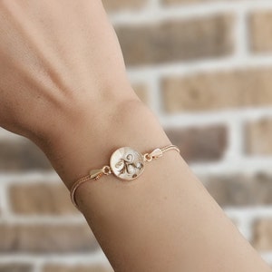 May include: A gold chain bracelet with a round pendant featuring a swirl design. The pendant is made of a white material with a gold trim.