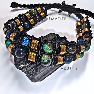 Può includere: Un braccialetto in cordoncino nero con perline dorate e perline di pietre preziose blu e verdi. Il braccialetto è esposto su una pietra nera con le parole "HÉMATITE" e "AZURITE" scritte su di essa.