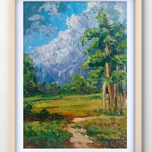 May include: Oil painting of a landscape scene with a bright blue sky filled with white clouds. The foreground features a green field and a path leading to the trees. The painting is framed in a light wood frame.