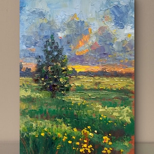 May include: An oil painting on canvas depicting a landscape with a single tree in a field of green grass and yellow flowers. The sky is filled with thick, textured brushstrokes in shades of blue, purple, and orange, suggesting a sunset scene.