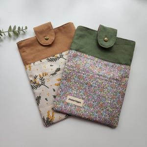 May include: Two fabric pouches. One is tan with a floral pattern and a brown flap with a brass snap. The other is olive green with a floral pattern and a green flap with a brass snap. The text "AtelierHippie" is on the floral pouch.
