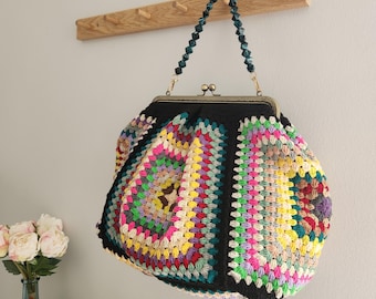 May include: A crochet handbag featuring a multi-colored granny square pattern with black borders. The bag has a bronze-toned metal kiss-lock frame and a handle made of dark teal faceted beads. The design incorporates various bright yarn colors.