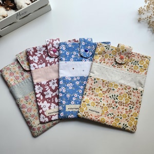 May include: Four floral fabric phone cases with snap closures. The cases feature various patterns, including white flowers on a burgundy background, blue flowers, and yellow flowers. Each case has a different color snap closure and a white accent stripe.